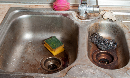 Steel dishwashing wool and dish sponge in a dirty metal sink. Unhygienic and unhealthy kitchen detail.