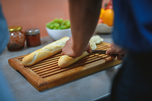 Hispanic woman is cutting baguette in a domestic kitchen. She is preparing breakfast for a family.