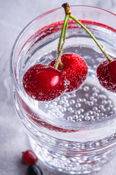 istock Fresh cold sparkling water drink with cherry, raspberry and currant berries in transparent glass on stone concrete background, summer diet beverage, angle view macro 1271605180
