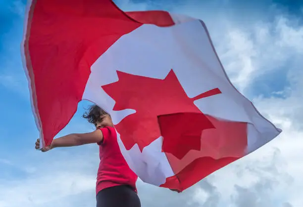 Nice girl of Asian descent celebrating Canada Day with a beautiful flag. Conceptual image about the ethnic diversity of Canada.
