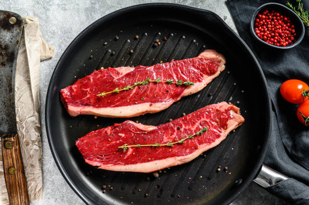 istock Raw marbled beef steak on a grill pan, ingredients for cooking. Gray background. Top view. 1271609885