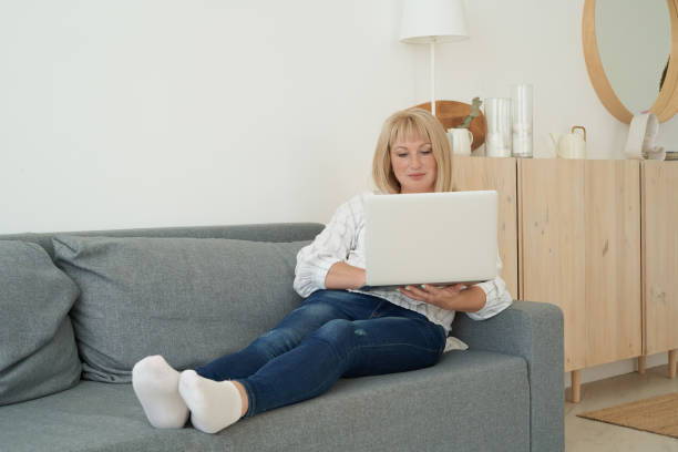 istock Mature woman using laptop while sitting on comfortable sofa, home interior 1271611357