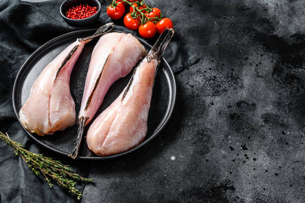Separate fresh monkfish without head and skin. Black background. Top view. Copy space