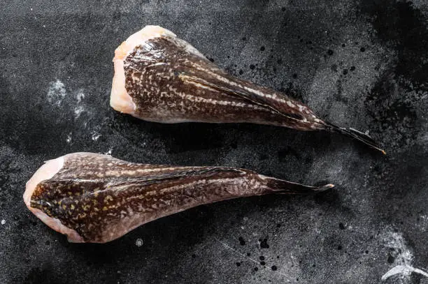 Fresh monkfish without a head. Black background. Top view.