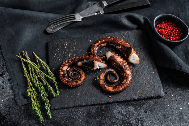 istock Fried octopus tentacles with thyme and pink pepper. Fresh seafood. Black background. Top view 1271613725
