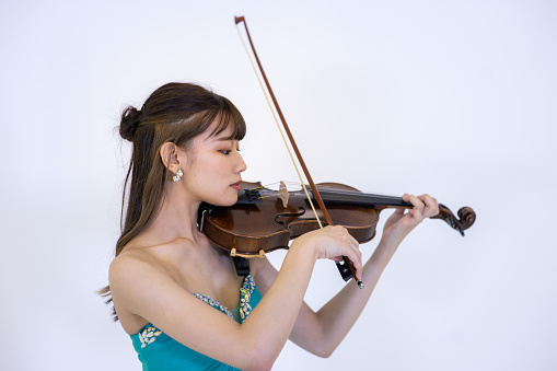 Young woman in turquoise blue dress playing violin against white background