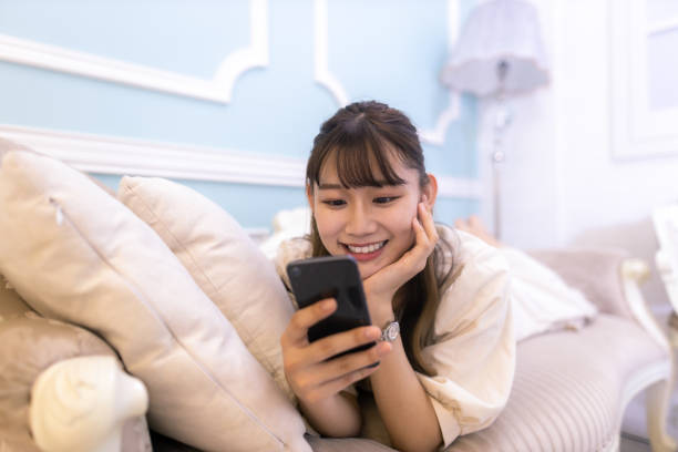幸せな若い女性はソファに横たわって、彼女の部屋でスマートフォンでメッセージを読む