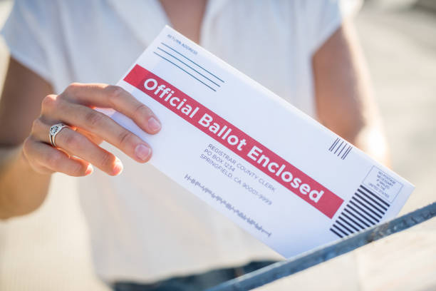 A young woman places her absentee voter ballot for the 2020 presidential election into a blue United States Postal mailbox.