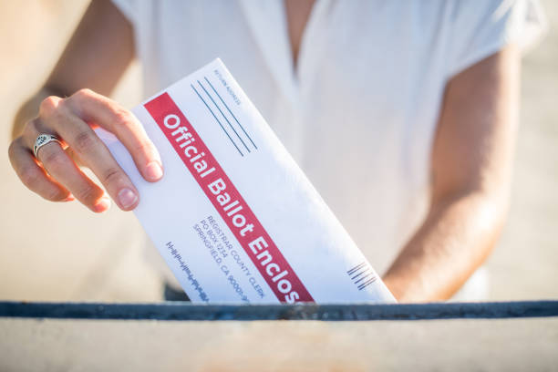 Woman Mailing Her Absentee Voter Ballot A young woman places her absentee voter ballot for the 2020 presidential election into a blue United States Postal mailbox. absentee ballot photos stock pictures, royalty-free photos & images