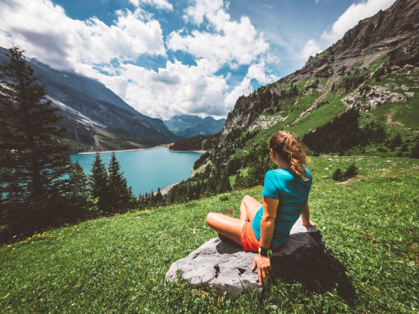 Woman hiking at Lake Oeschinensee, sitting down enjoying the view Woman hiking in the mountains by the Oeschinen lake in Berner Oberland region in central Switzerland.  Hiker hiking in Swiss alps in the summer. lake oeschinensee stock pictures, royalty-free photos & images