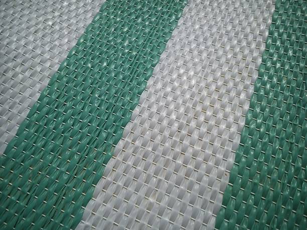 Green and white synthetic burlap, close-up. Polyethylene material. Interlacing of polyethylene fibers and threads. Beach mat or sports mat.