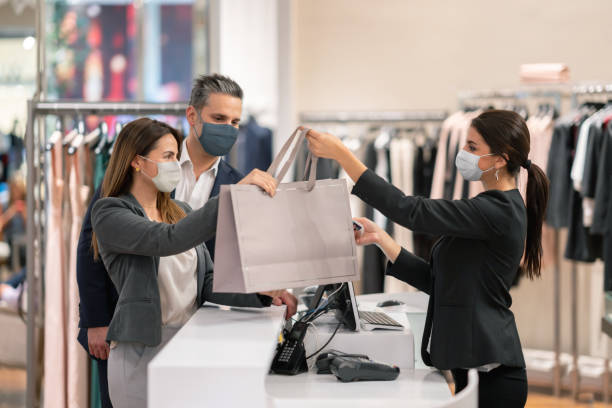 пара покупки в магазине одежды и использование facemasks во время пандемии - retail стоковые фото и изображения