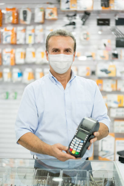 istock Salesman at a hardware store wearing a facemask and holding a credit card reader 1271626564