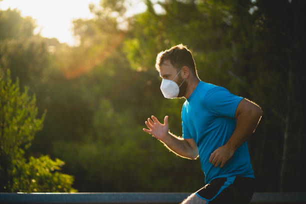 giovane che indossa una maschera chirurgica ffp2 corre su una strada durante il tramonto circondato dalla natura a maiorca (spagna) - sports clothing practicing success vitality foto e immagini stock