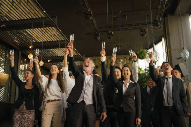 企業のアニバーサリーなどの特別なイベントで友情とチームワークを祝うために一緒にワインやシャンパンのグラスを乾杯ビジネスパーティーを持っている企業のビジネスマン - party business toast champagne ストックフォトと画像