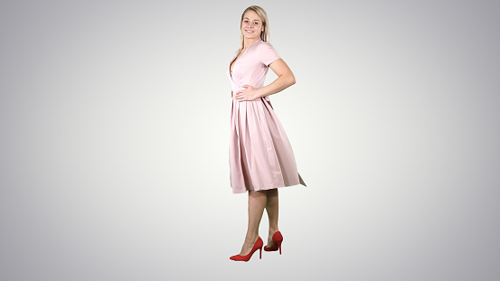 Full length portrait. Woman in a pink dress making a turn and looks at her self like in the mirror on gradient background. Professional shot in 4K resolution. 005. You can use it e.g. in your commercial video, business, presentation, broadcast