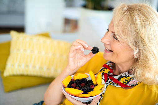 Healthy senior woman eating healthy fruit salad in the living room.