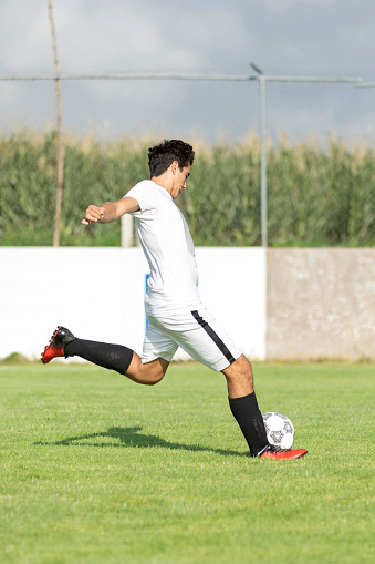 Young soccer player shooting the ball in grass field