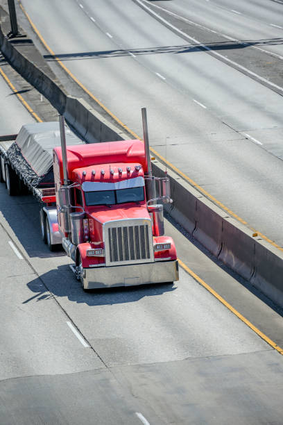 istock Powerful bright red classic big rig semi truck transporting covered commercial cargo on flat bed semi trailer running on the divided multiline highway road intersection 1271640704