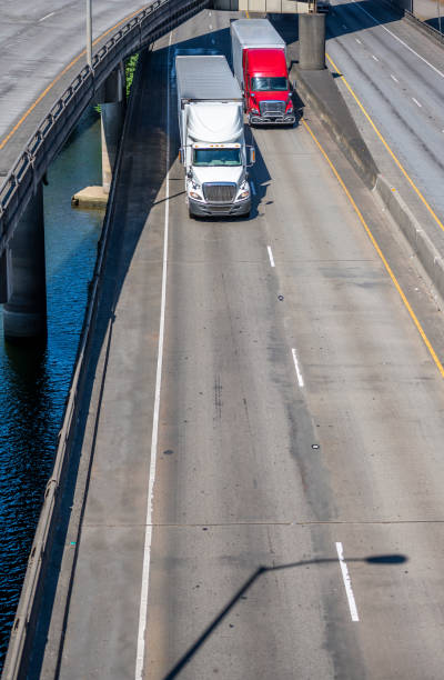 istock Different two big rigs semi trucks with semi trailers running side by side on the overpass road intersection along the river 1271641113