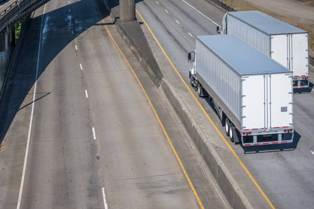 istock Two different big rig semi trucks with semi trailers moving on the wide divided highway road with overpass road intersection 1271641128