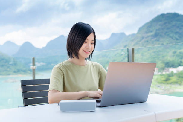 una freelance asiática que usa un portátil para trabajar al aire libre en el viaje - lake asia young women beautiful people fotografías e imágenes de stock