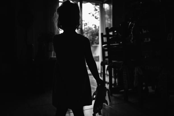 무서운 벽에 그녀의 손에 그녀의 헝겊 인형과 빛에 대한 어린 소녀. 할로윈 공포 개념 - surprise shouting child black and white 뉴스 사진 이미지