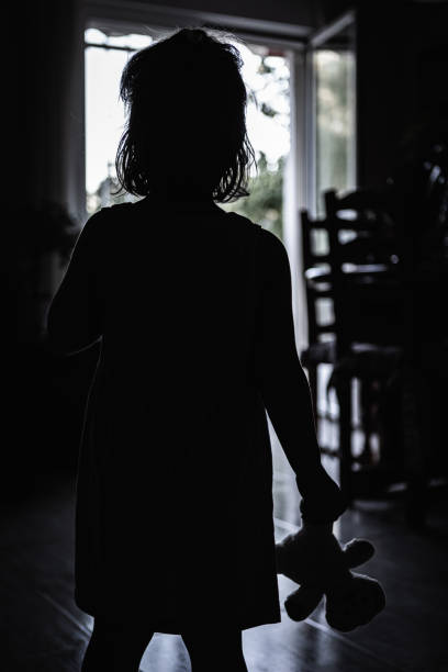 niña contra la luz con su muñeca de trapo en la mano en una pared de miedo. concepto de terror de halloween - surprise shouting child black and white fotografías e imágenes de stock