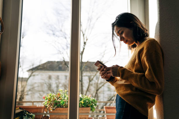 istock Woman using smart phone by window at home 1271666463