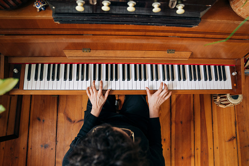 High angle view of woman practicing upright piano. Female is playing keyboard instrument at home. She is in living room.