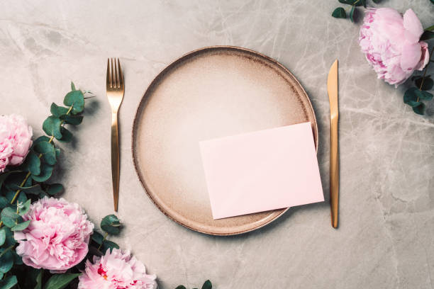 istock Flower arrangement on table served for festive dinner with copy space for your text, invitation. Greeting card. Top view. Peony, eucalyptus, plates, golden cutlery, wineglasses on marble background 1271666810