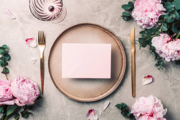 istock Flower arrangement on table served for festive dinner with copy space for your text, invitation. Greeting card. Top view. Peony, eucalyptus, plates, golden cutlery, wineglasses on marble background 1271666823