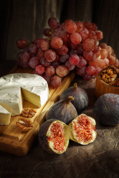 autumn atmospheric still life with figs, french brie cheese, pink grapes and walnuts. the light pattern emphasizes even the smallest details. food poster. - close to food and drink yummy food imagens e fotografias de stock