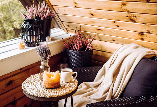 Lindo arreglo de decoración del hogar de otoño. Pequeño balcón de cabaña de madera con flores de brezo en maceta, lavanda en jarrón de botella, llama a la luz de las velas, suave color beige a cuadros esperando en una cómoda silla de muebles de jard photo