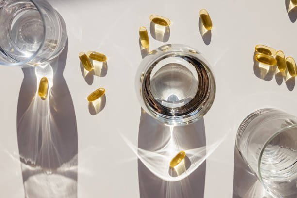 istock Omega 3 capsules and glasses with water on white table. 1271676665