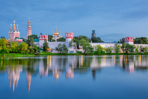 Novodevichy monastery with a reflection in the lake at sunset. The famous Moscow landmark with Golden domes and a reflection of the landscape on the water of the Park pond against the background of a picturesque blue sky with clouds.