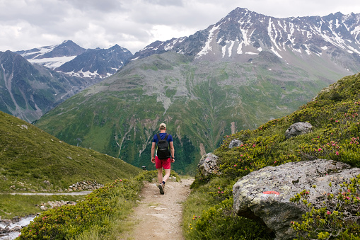 July 21, 2020 - Rifflsee, Austria: Man in red shorts walking on a path next to a stream in the mountains with amazing scenery below him - hiking vacations Alps in Austria.