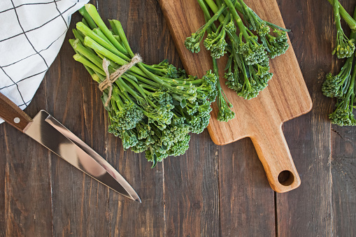 Raw green broccolini vegetable on wooden table. Overhead view.