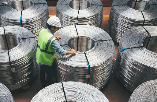 Overview of young quality inspector man checking production line and testing quality of steel pipe coils at warehouse section in cable factory. XXXL