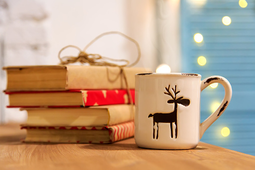 Winter tea. Winter books. A cup of hot tea, books, Christmas shining garland on a wooden background. Winter holidays.