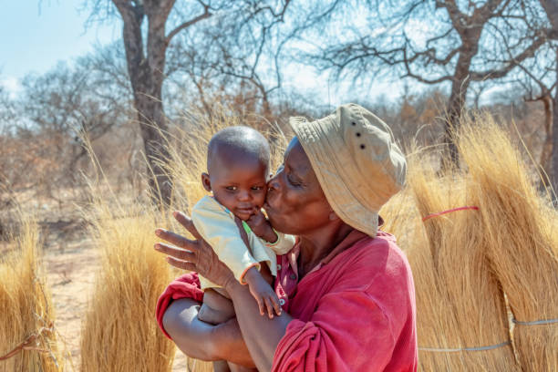 後ろに彼女の子供を運ぶ村のアフリカの女性 - africa child village smiling ストックフォトと画像