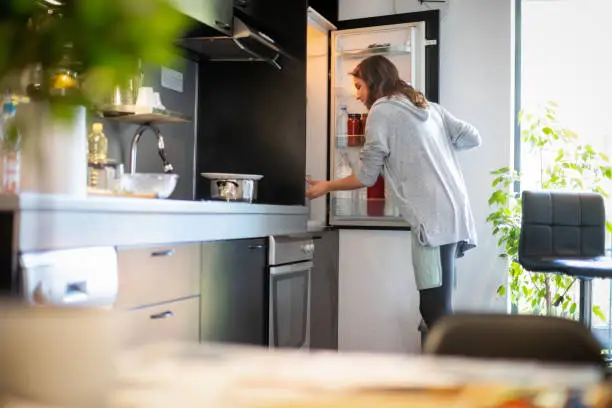 Mid adult woman opening the fridge to find food and prepare lunch for her family