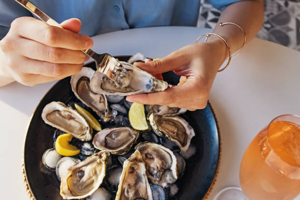 Woman eating fresh oysters with lemon close-up. Woman eating fresh oysters with lemon close-up. Table with big plate of oysters and pink sparkling wine in a glass oyster photos stock pictures, royalty-free photos & images