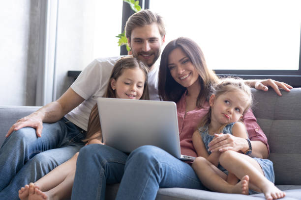 istock Smiling parents and kids using laptop on sofa at home, enjoying funny video at computer 1271688377