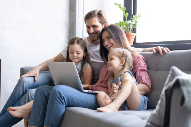 istock Smiling parents and kids using laptop on sofa at home, enjoying funny video at computer 1271688990