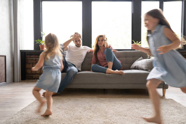 istock Tired mother and father sitting on couch feels annoyed exhausted while noisy daughters shouting run around sofa 1271689030