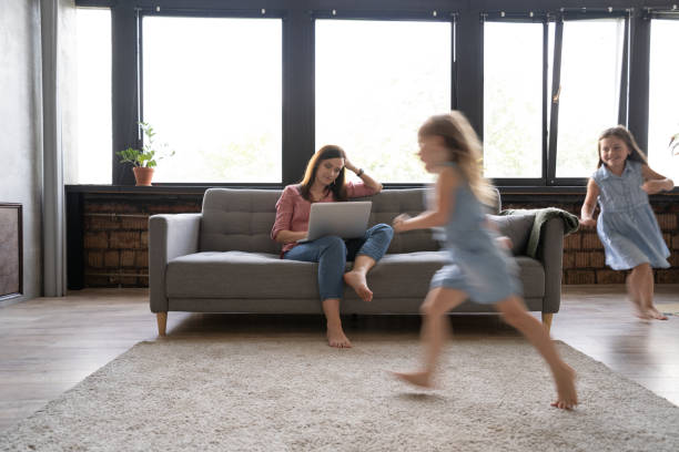 istock Young single mother working on laptop in loft sitting on couch while her daughters running around her and shouting. 1271689502