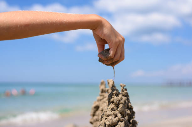 A child's hand builds a sandy figure on the beach. In the background the sea. Construction concept.