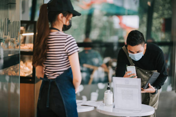 asian chinese cafe waitress checking body temperature for client as standard procedure and check in process before entering cafe as new normal