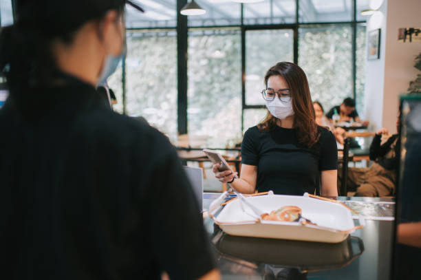 istock asian chinese beautiful woman making payment through contacless payment using her mobile app at the cashier with face mask in cafe 1271696330